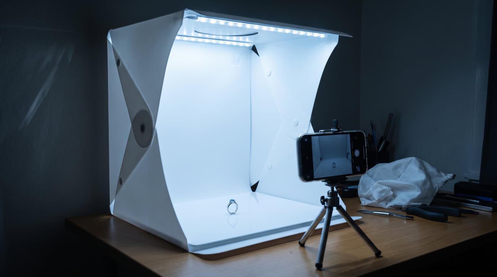Smartfon fotografujący naszyjnik w małym namiocie bezcieniowym z taśmami LED, dającymi płaskie światło.
